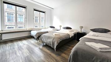 A modern hotel room with two beds, a large window with a city view, and a wooden floor.