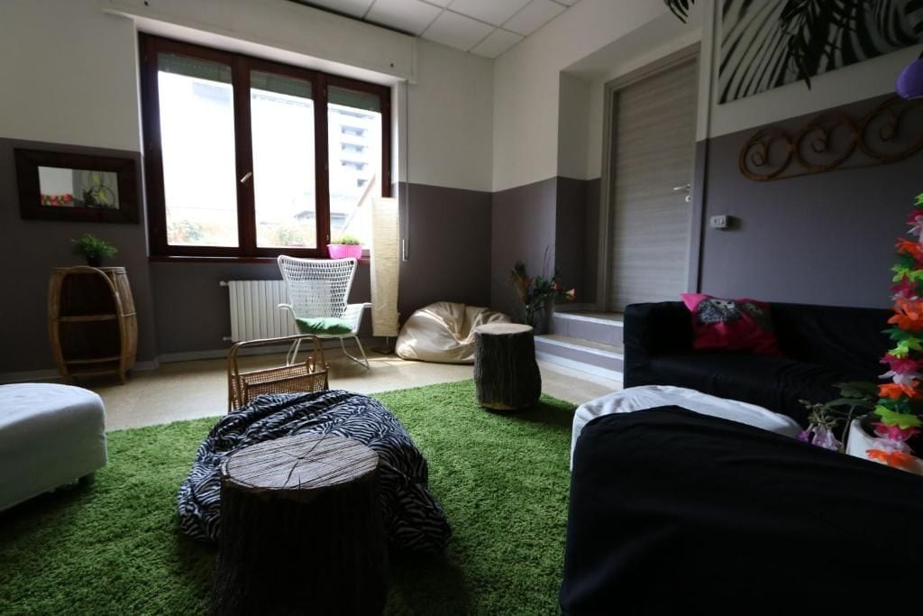 A room with a large window, a white chair, a black sofa, and a green carpet.