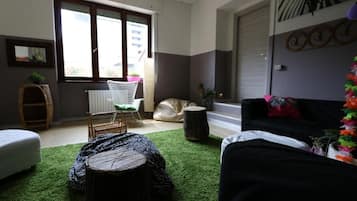 A room with a large window, a white chair, a black sofa, and a green carpet.