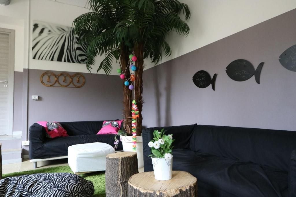 A modern living room with a black sofa, a white pouf, a wooden tree stump, and a decorative plant.