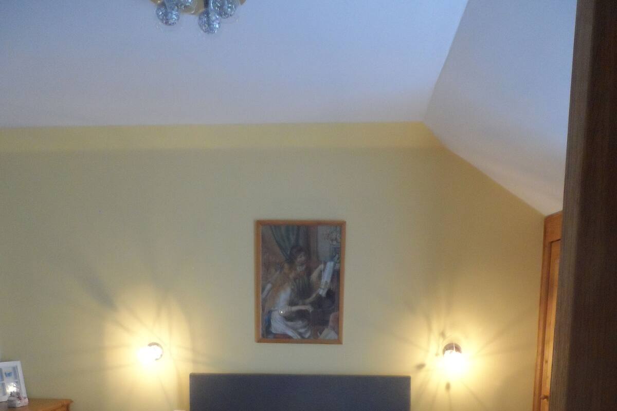 Un lit bien fait, avec deux oreillers et des serviettes pliées, deux tables de chevet avec des lampes, une commode en bois et un tableau accroché au mur.