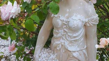 A statue of a woman holding grapes, surrounded by pink roses and greenery.