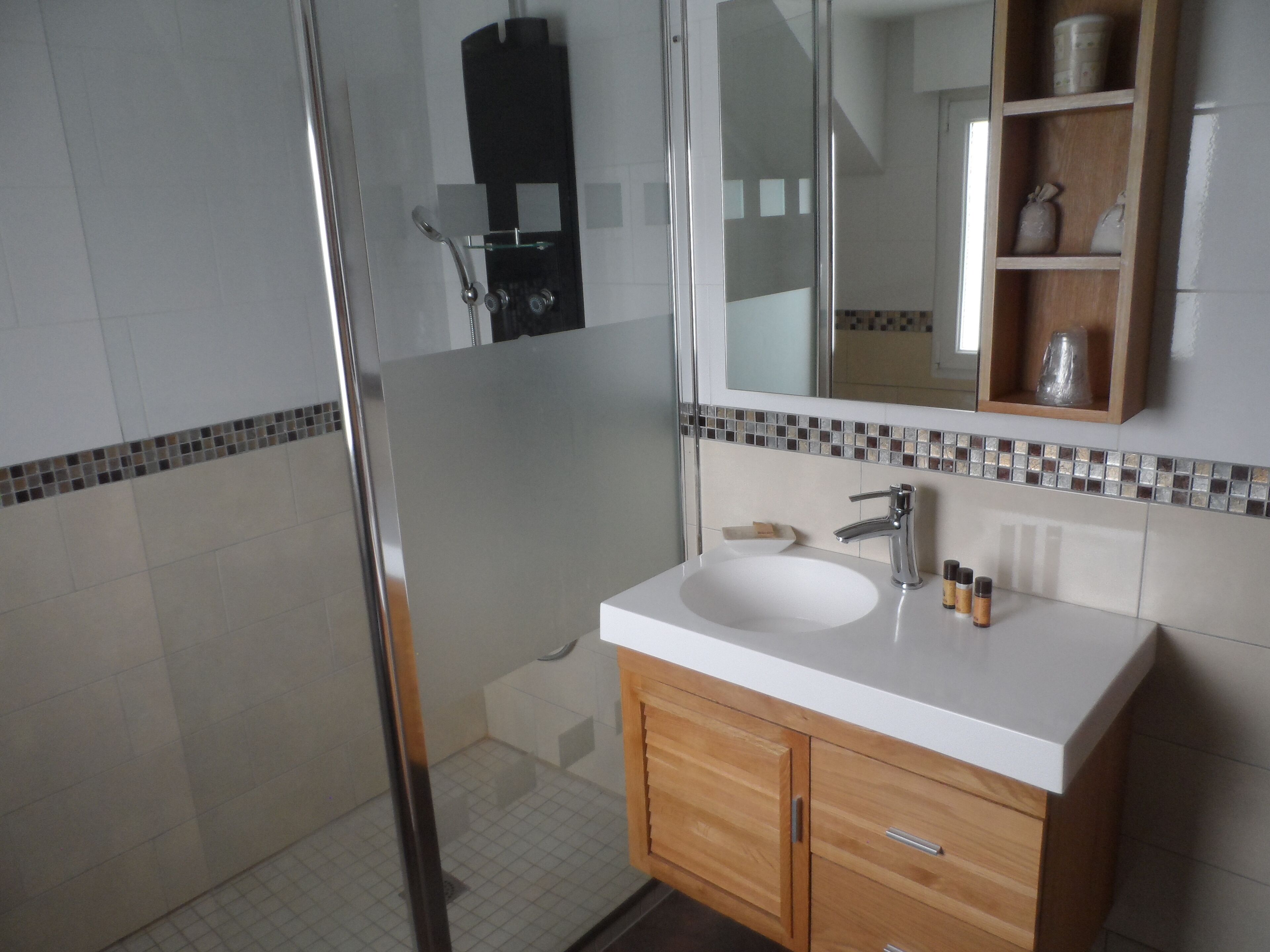 A bathroom with a glass shower enclosure, a white sink, and wooden cabinets.