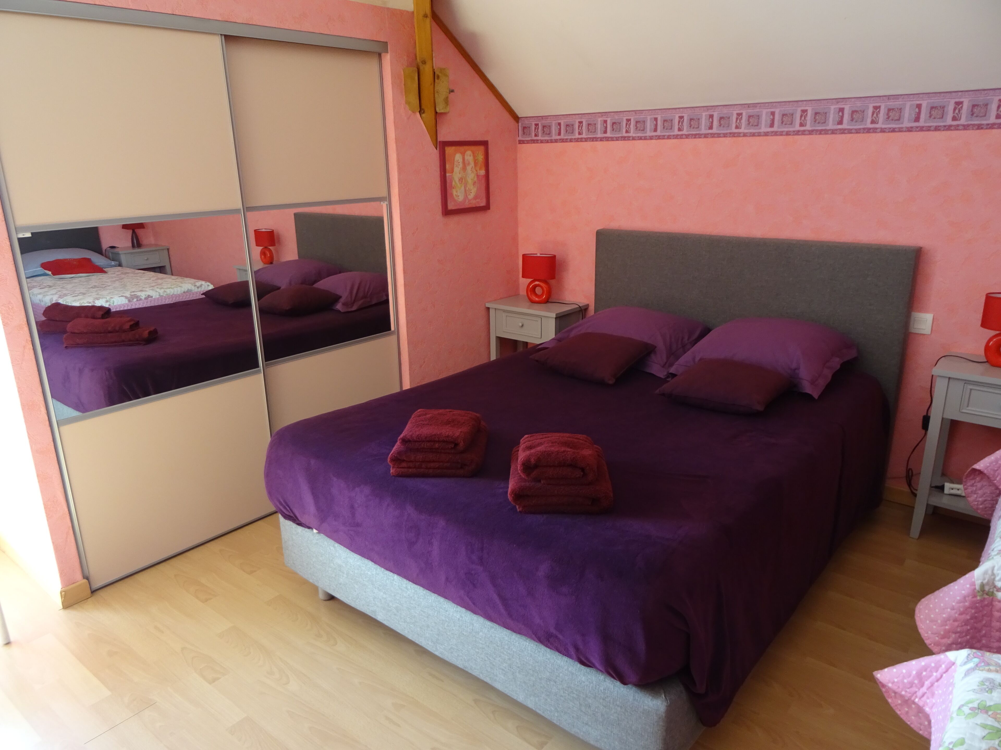 A bedroom with a large bed, two nightstands, a mirror, and a wooden floor.
