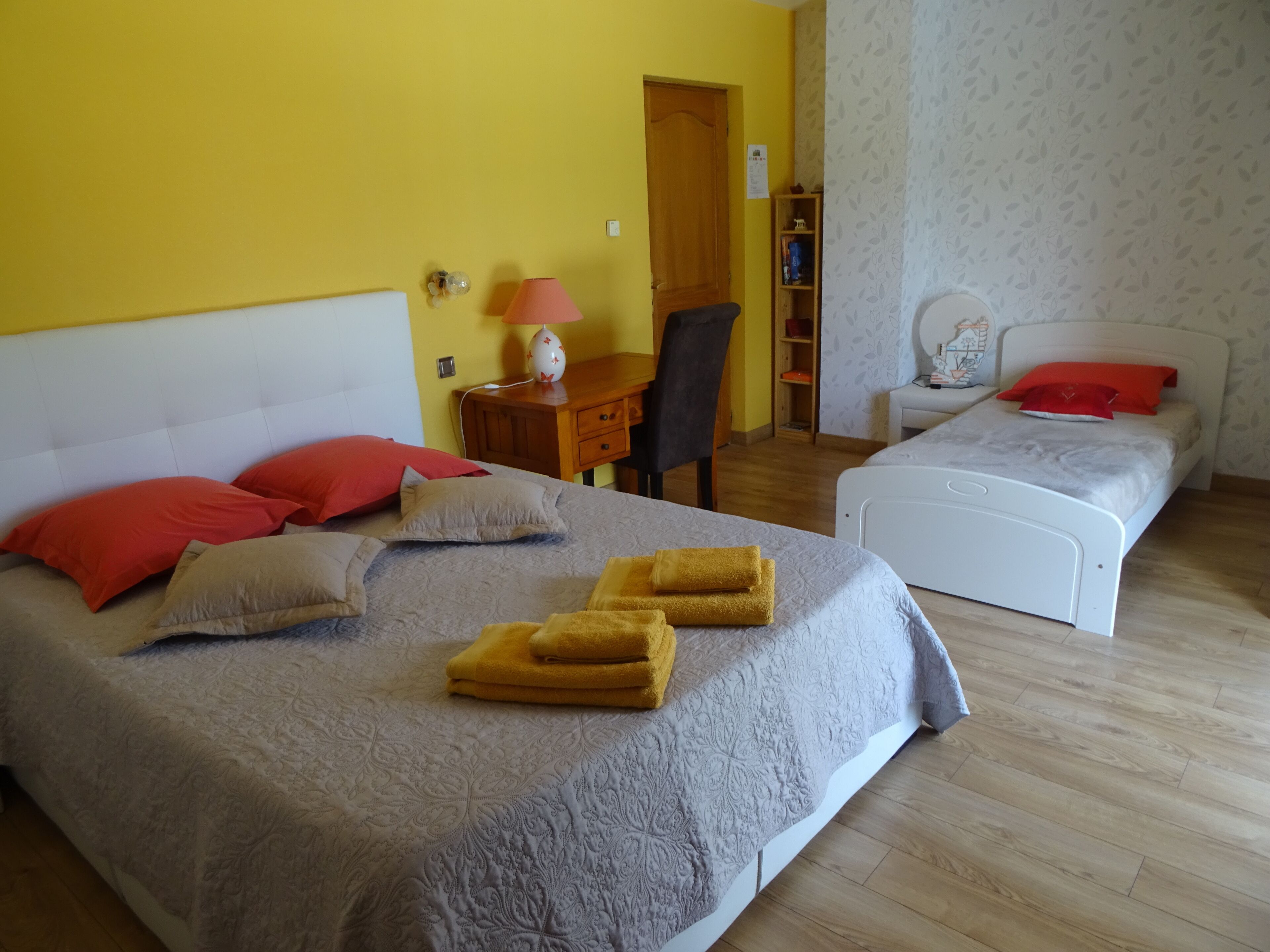 Une chambre d’hôtel avec un grand lit, un lit plus petit, un bureau avec une lampe et une chaise.