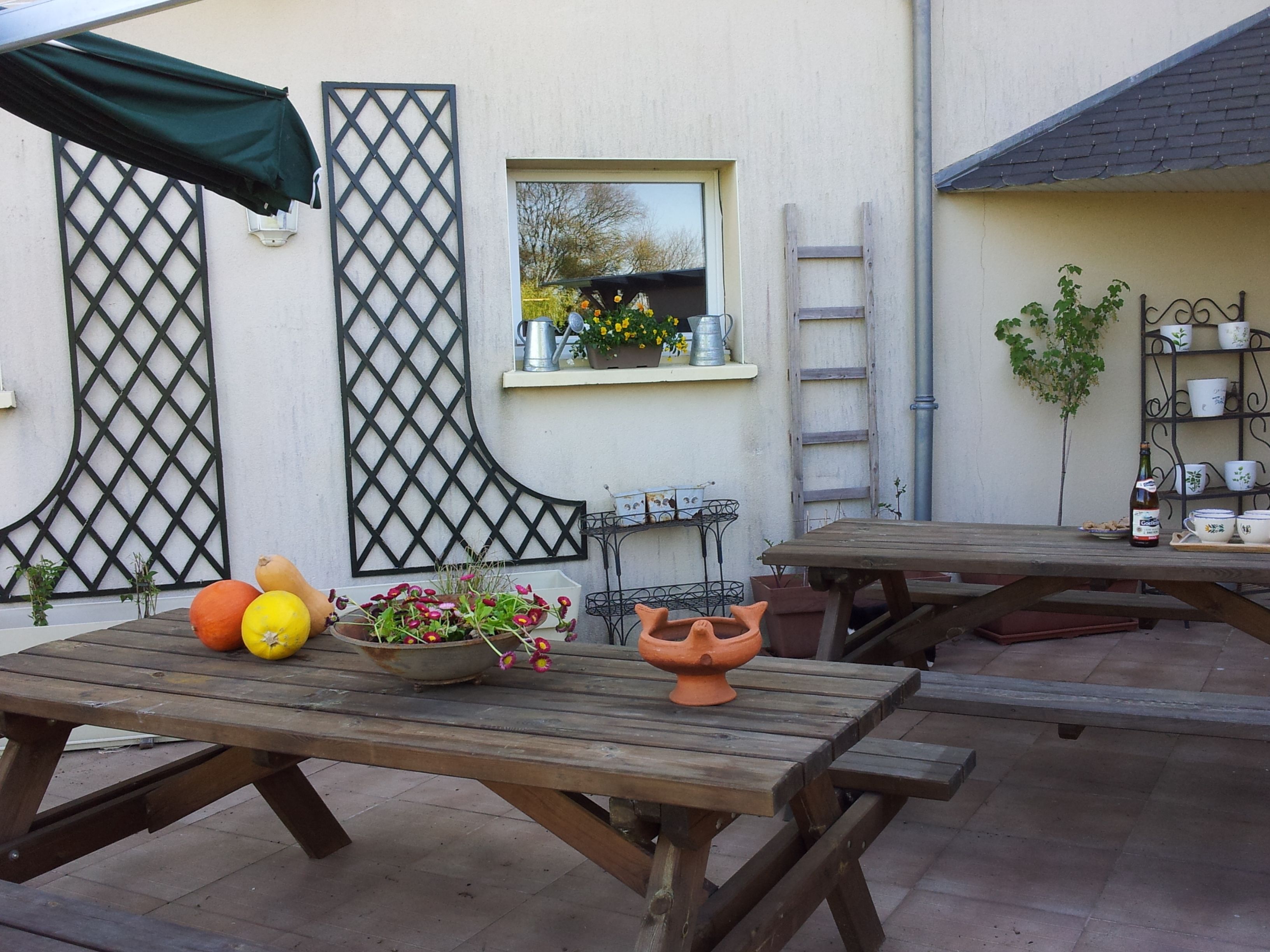 An outdoor patio area with wooden tables, a green umbrella, and potted plants.