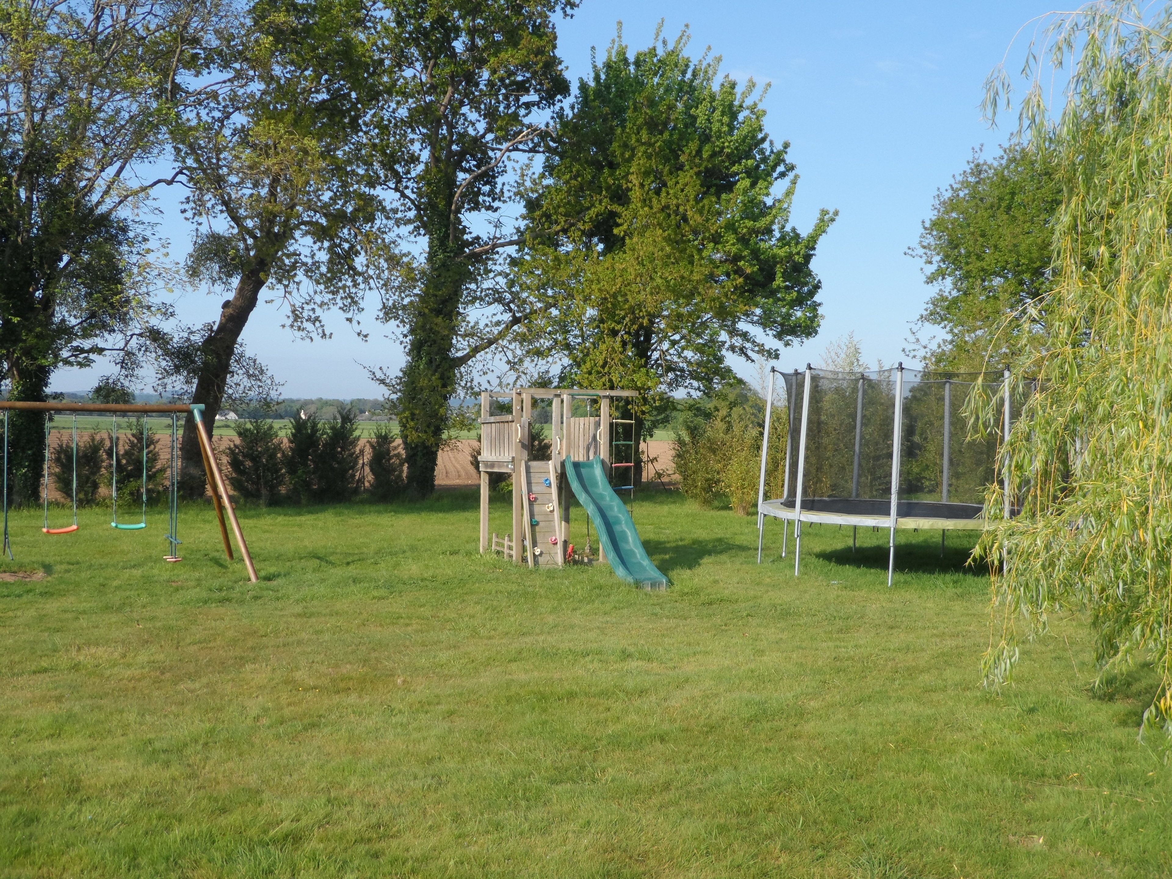 A playground with swings, a slide, and a trampoline in a grassy area with trees.