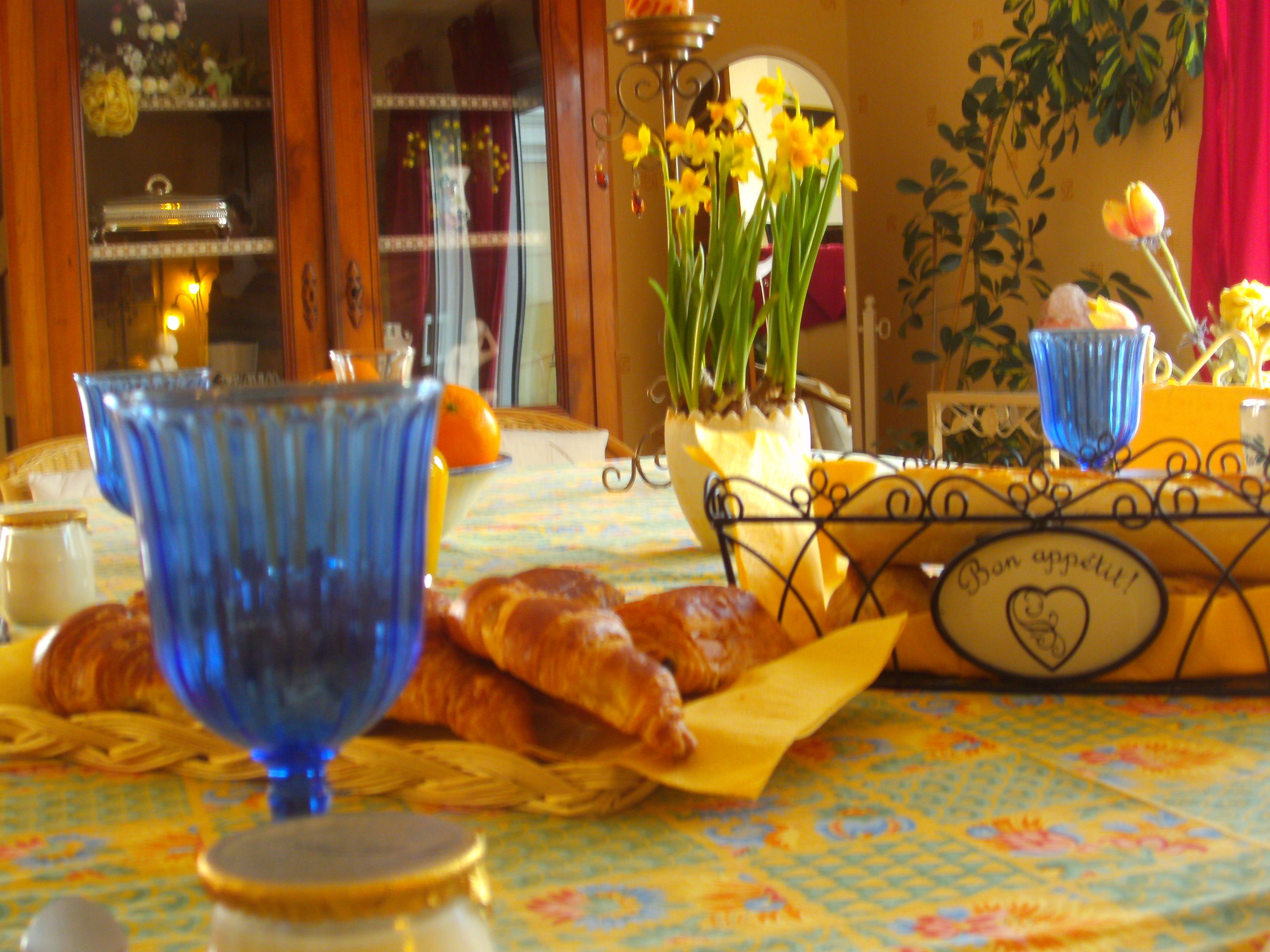 A breakfast setting with croissants, a blue glass, and a vase with flowers.