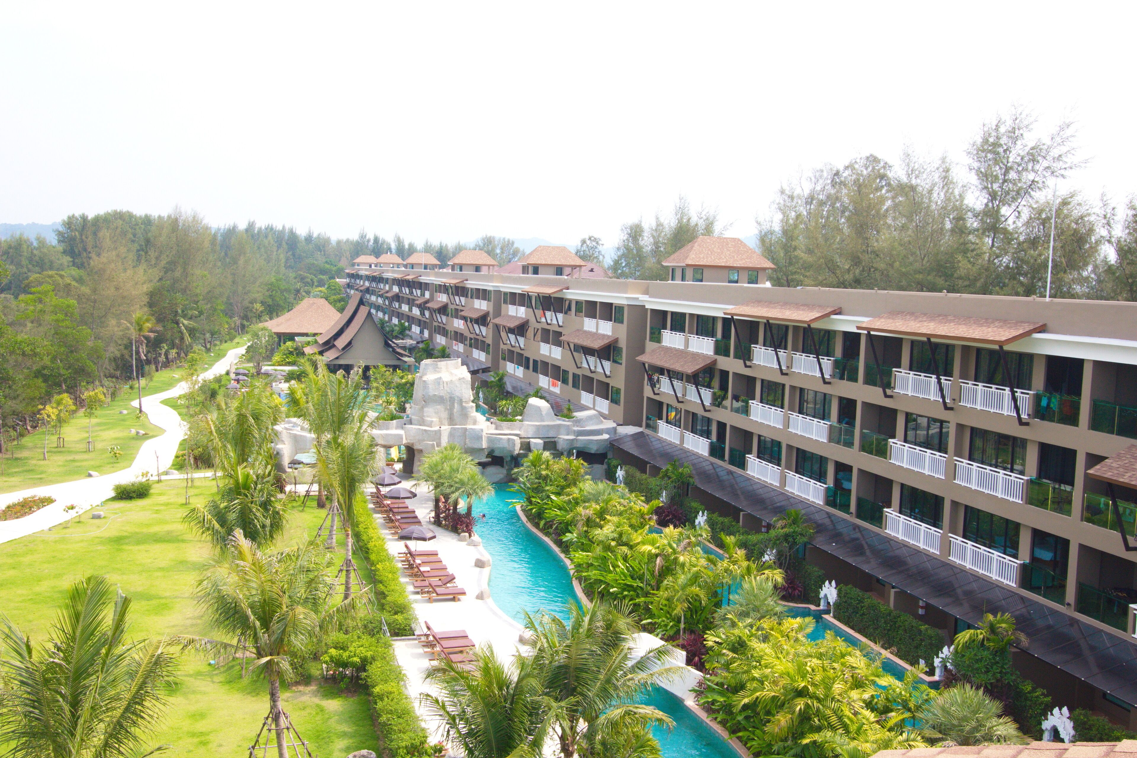 A hotel with multiple floors, a swimming pool, and lush greenery.