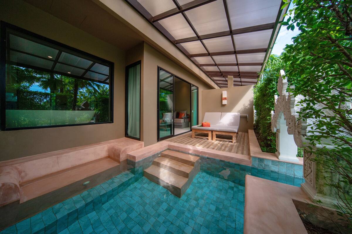 Uma área moderna com piscina ao ar livre, com escadas de acesso à água, um banco de madeira e vista para o verde ao redor.