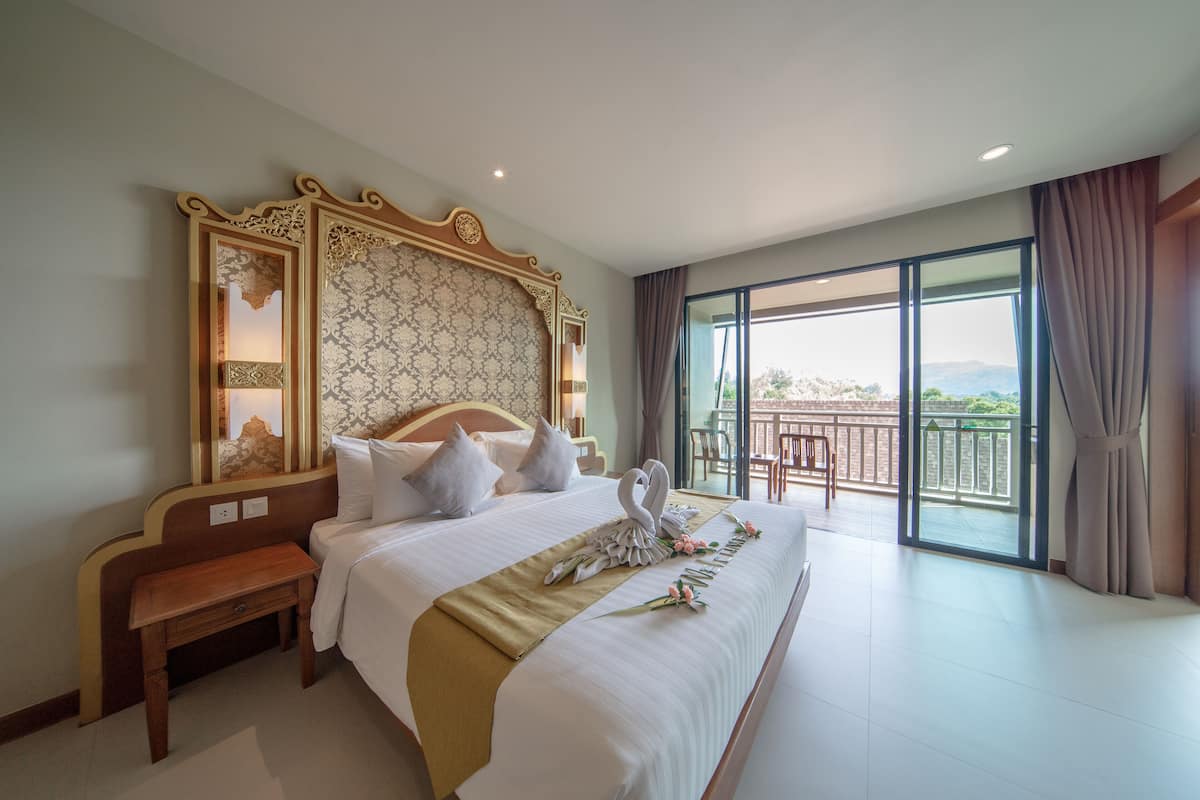 Uma cama grande com cabeceira decorativa, mesa de cabeceira de madeira e vista para o exterior através de uma grande janela.