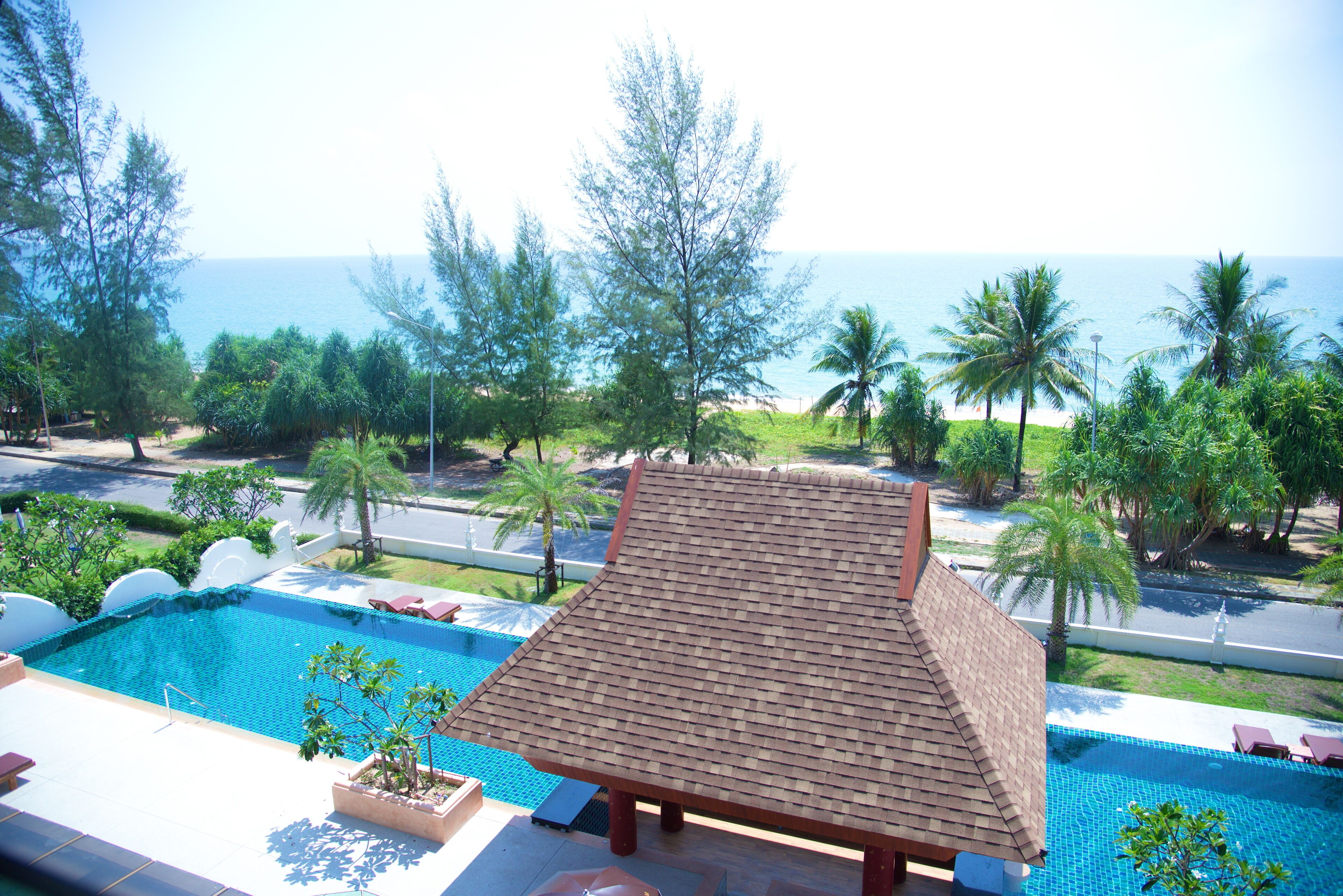 A swimming pool with a tiled roof, surrounded by lush greenery and a view of the ocean.