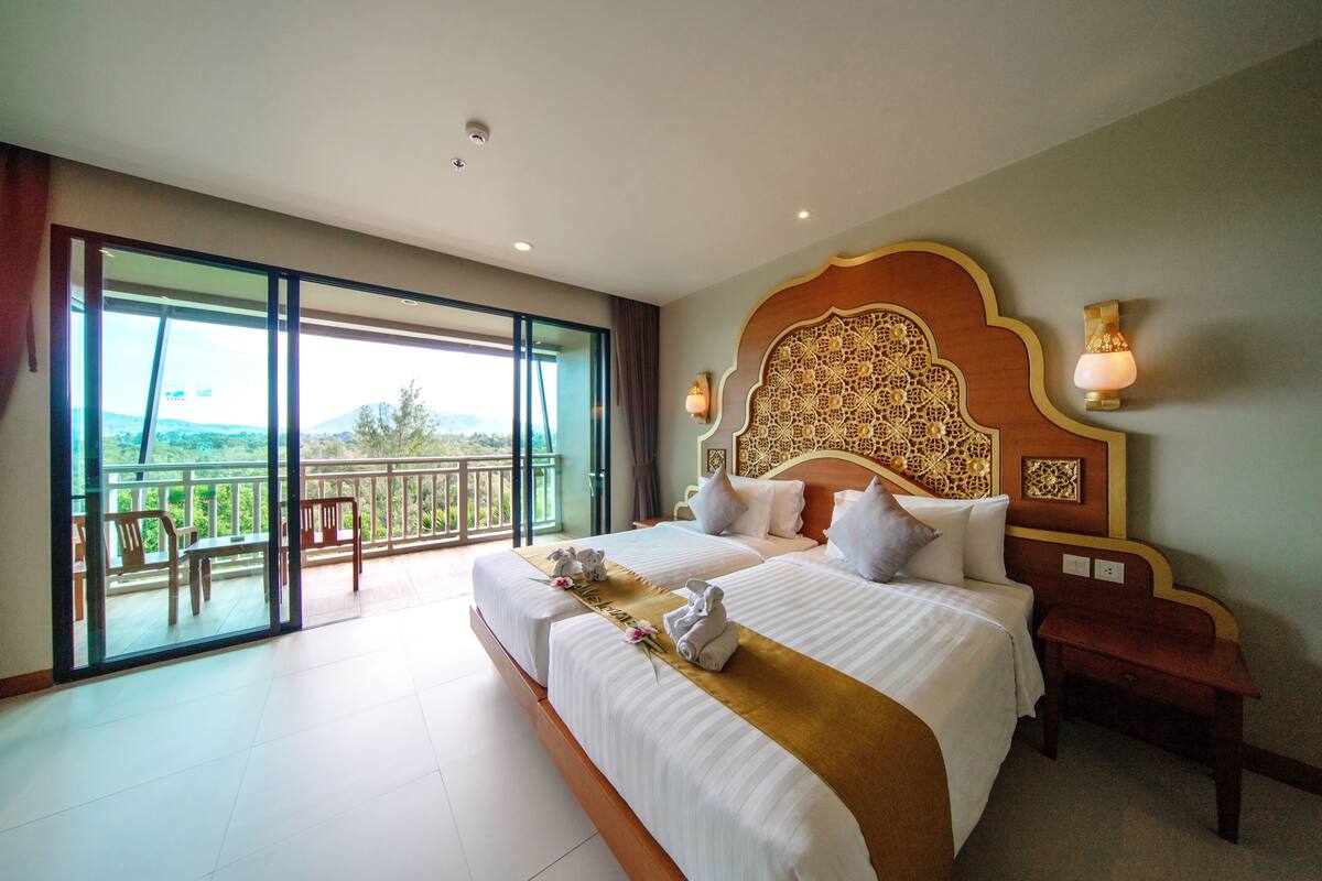 Quarto de hotel com uma cama grande, uma varanda com cadeiras e vista para o exterior.