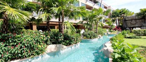Una piscina rodeada de abundante vegetación y un edificio de varios pisos con balcones.