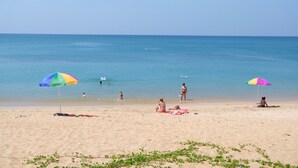 A beach with two colorful umbrellas, a sandy shore, and people enjoying the water. - Maikhao Palm Beach Resort (Mai Khao)