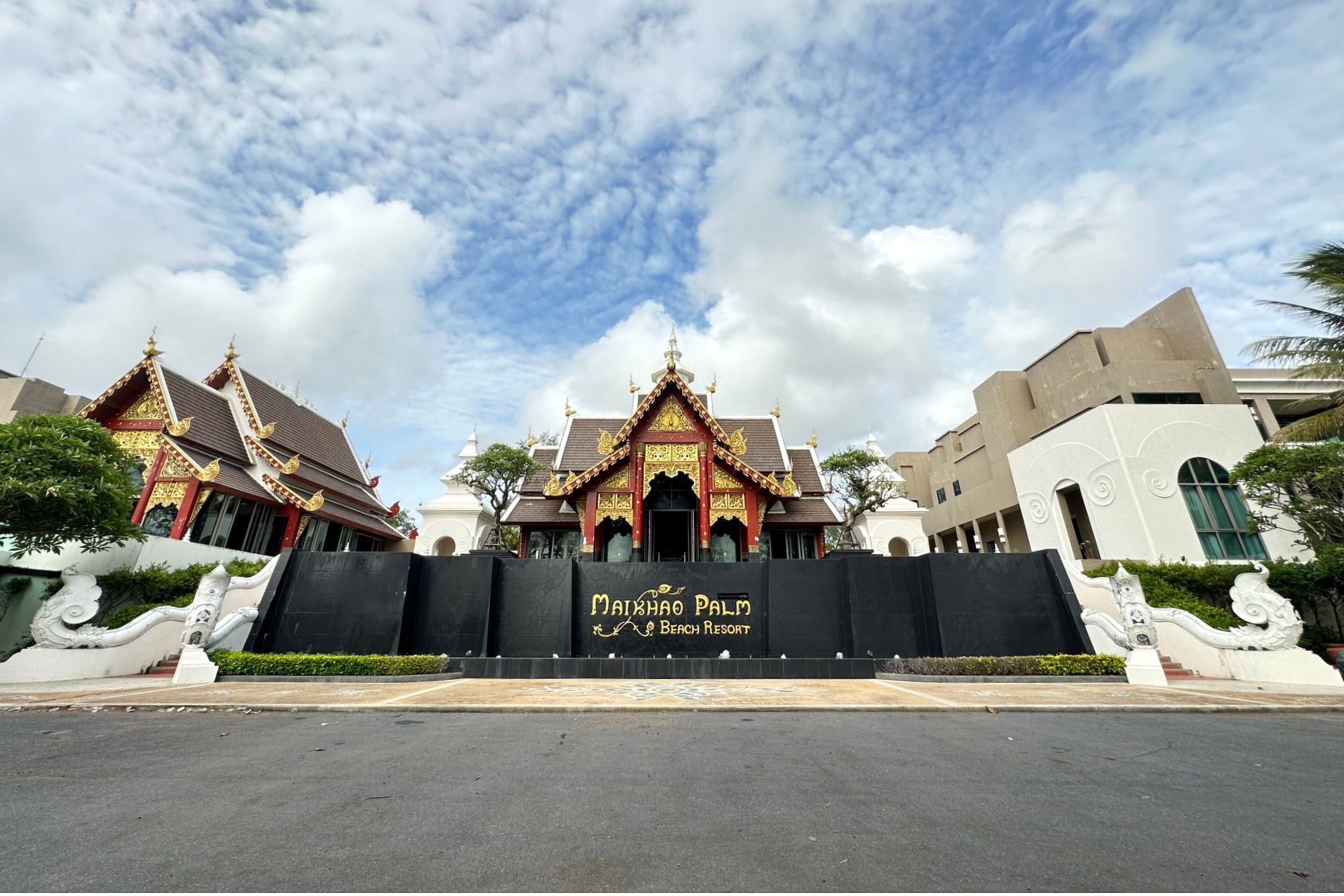 A resort entrance with traditional Thai architecture, a black gate, and a clear sky.