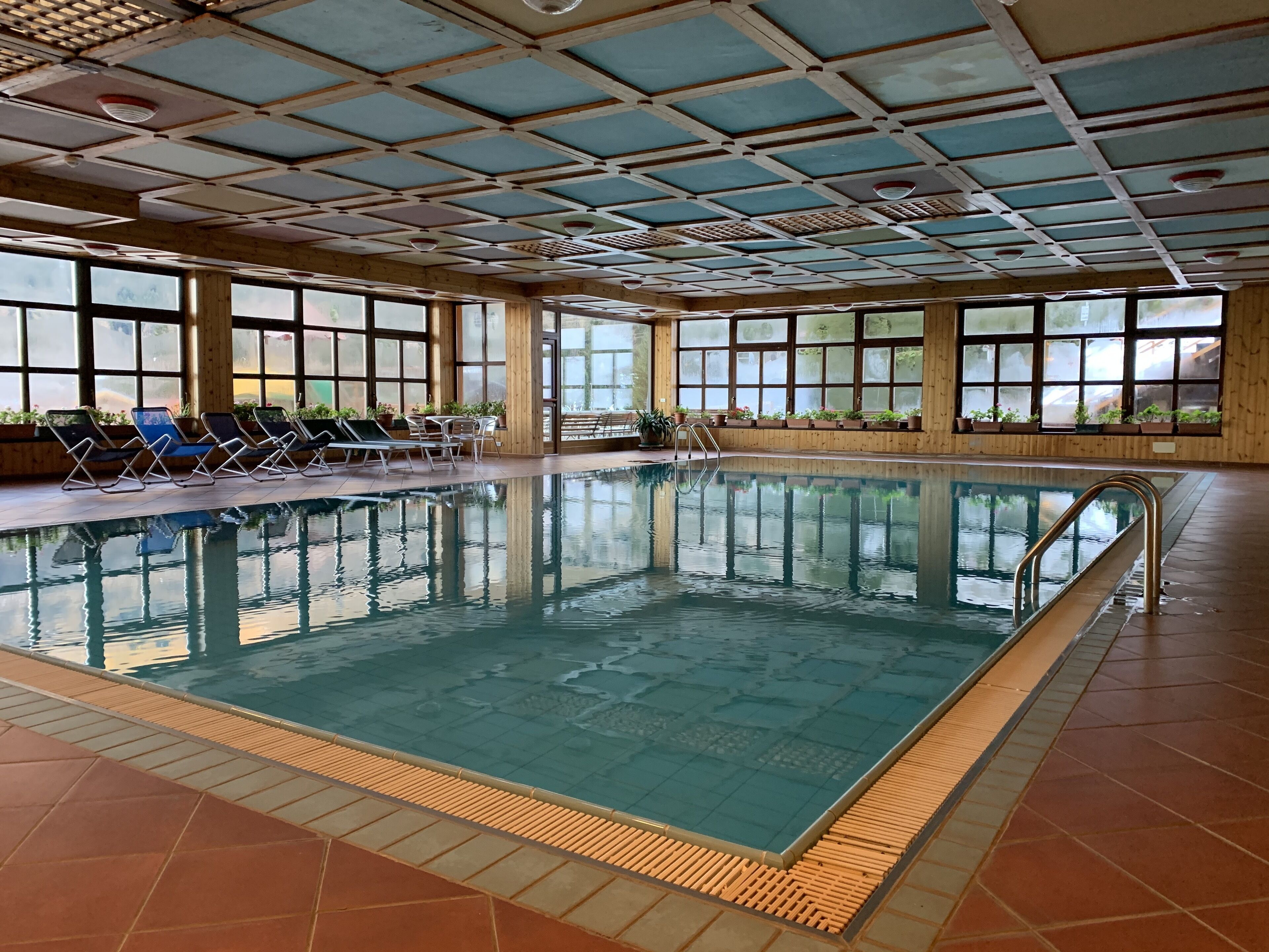 An indoor swimming pool with clear water, surrounded by lounge chairs and potted plants.