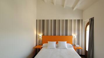 Ein Hotelzimmer mit einem großen Bett, gestreifter Tapete, einem orangefarbenen Kopfteil, zwei Nachttischen mit Lampen und einem Fenster mit Vorhängen.