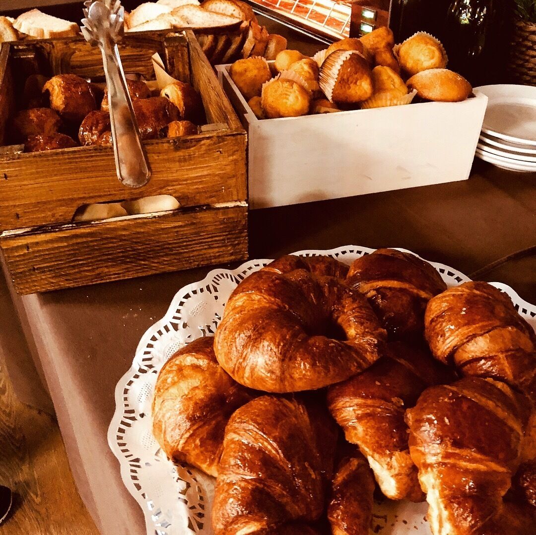 A buffet table with various baked goods, including croissants and pastries, arranged on a lace doily.