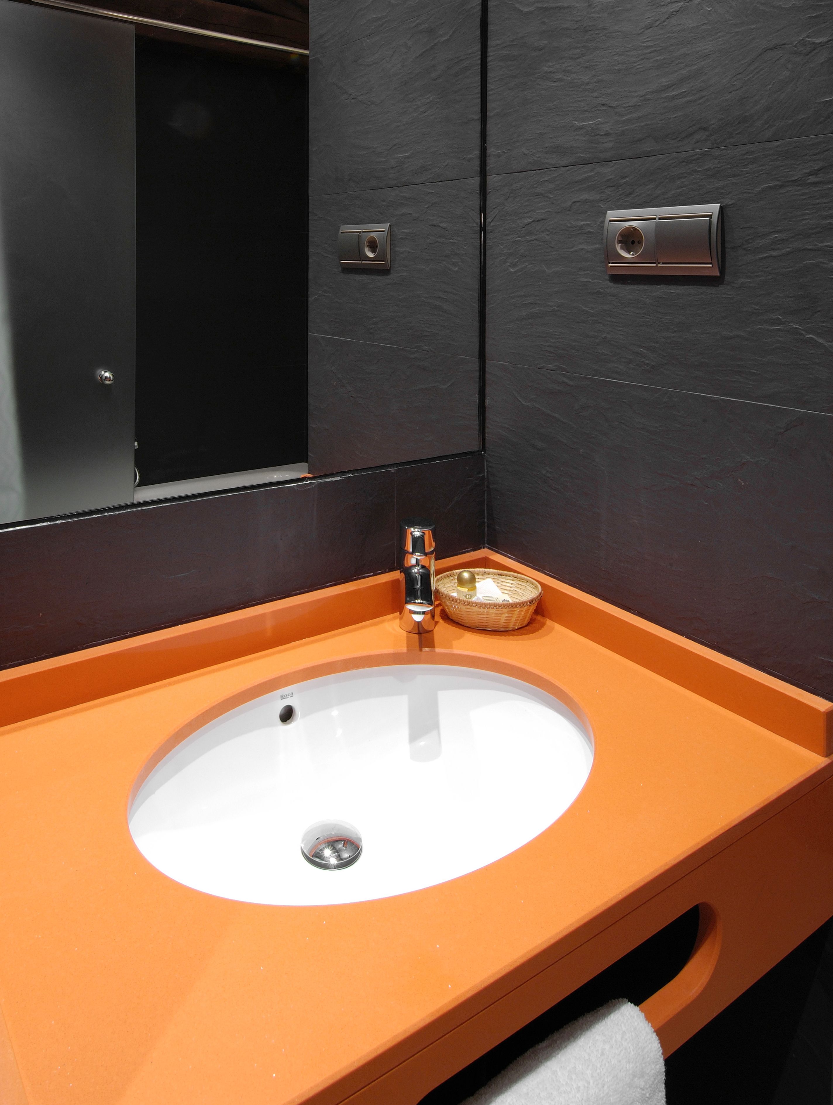 A bathroom with a white sink, orange countertop, and dark wall.