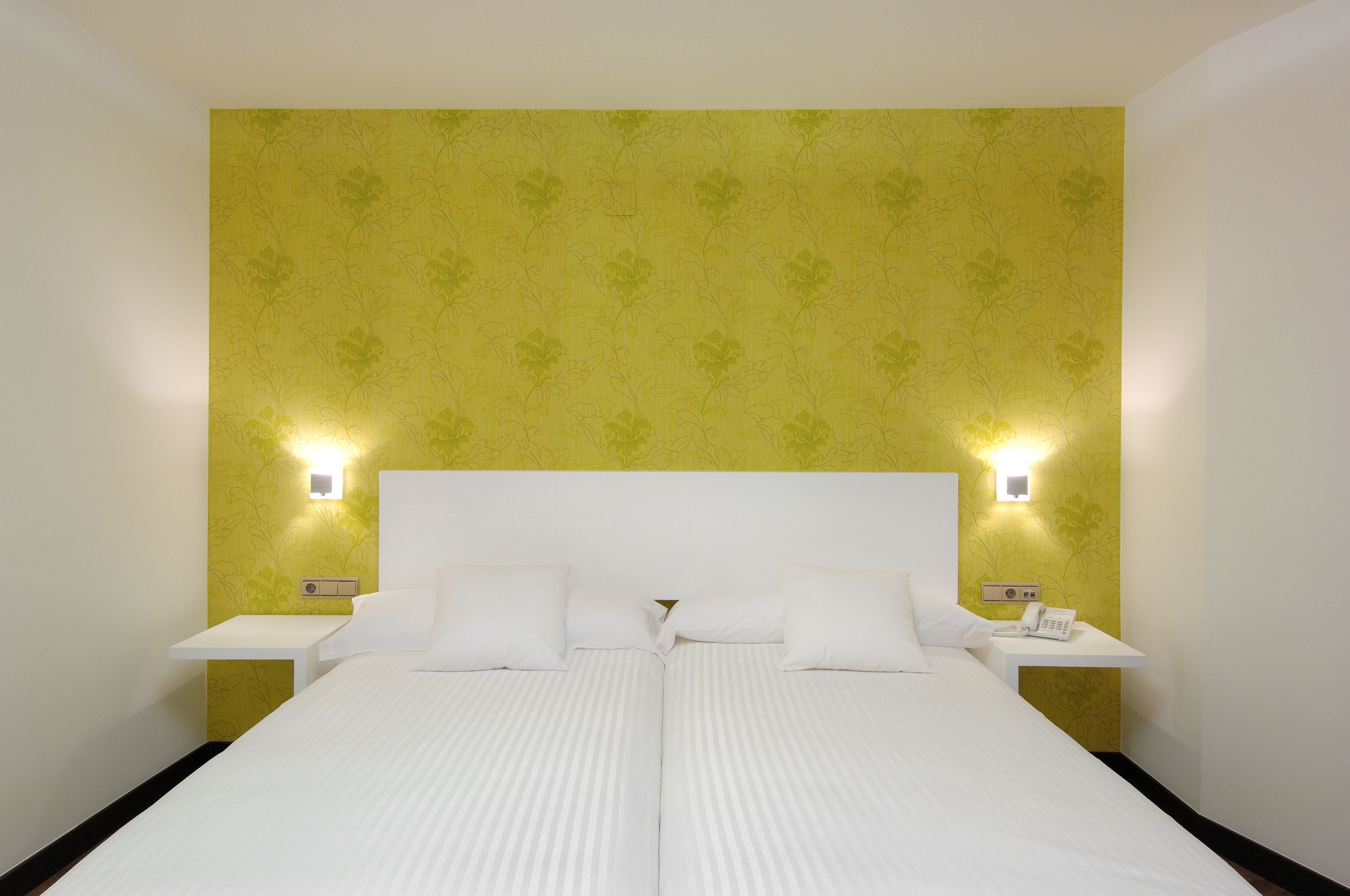 Ein Doppelbett mit weißen Bettwäsche, zwei Nachttische mit Lampen sowie gelber Blumenwallpaper.