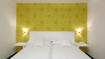 Ein Doppelbett mit weißen Bettwäsche, zwei Nachttische mit Lampen sowie gelber Blumenwallpaper.