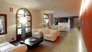 A spacious lobby with leather sofas, a reception desk, and a large arched window. - Hotel Cienbalcones (Daroca)