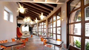 A spacious dining area with high ceilings, large windows, and modern orange chairs. - Hotel Cienbalcones (Daroca)