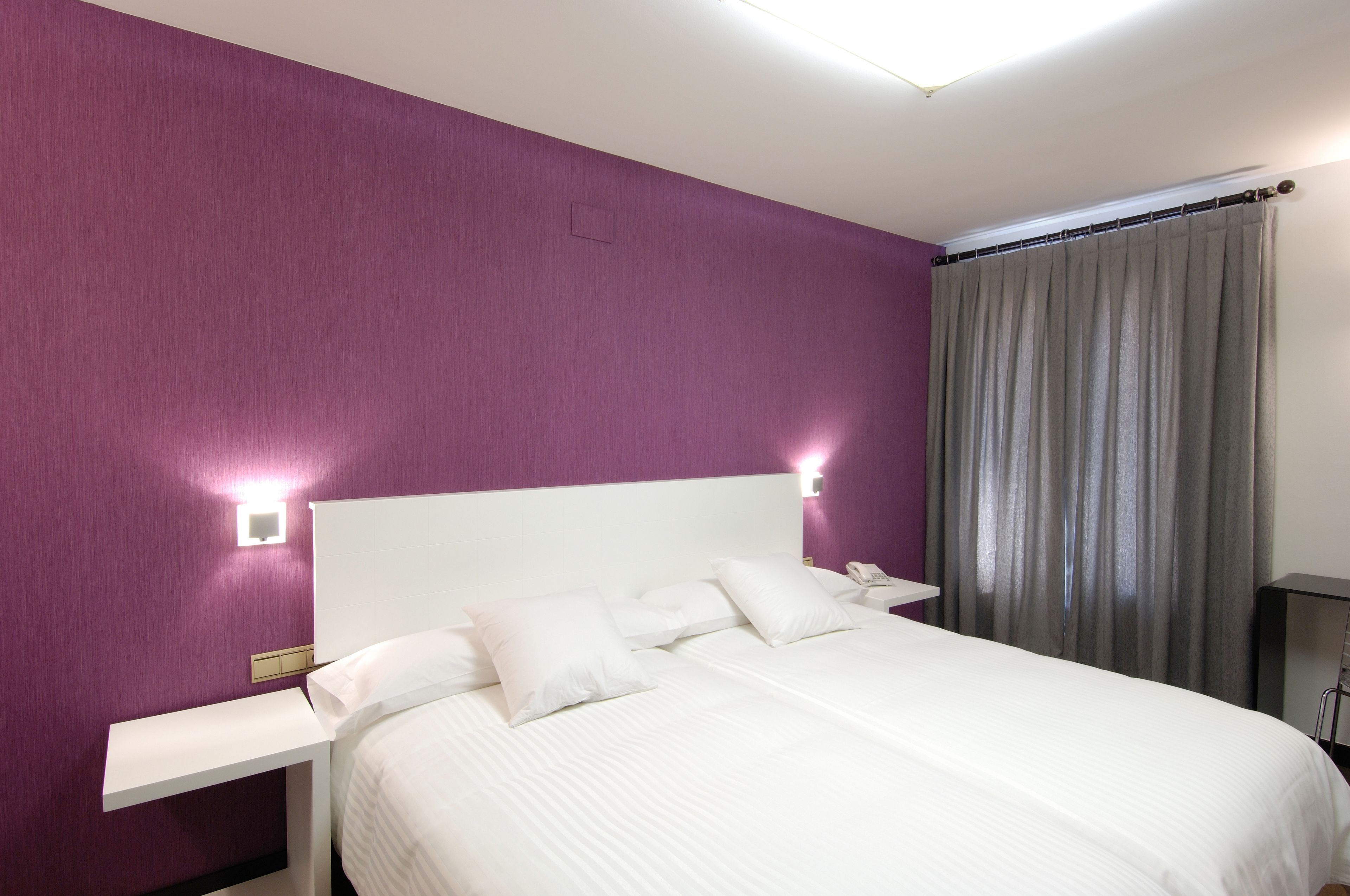 A hotel room with a large bed, white headboard, two bedside tables, and a nightstand.