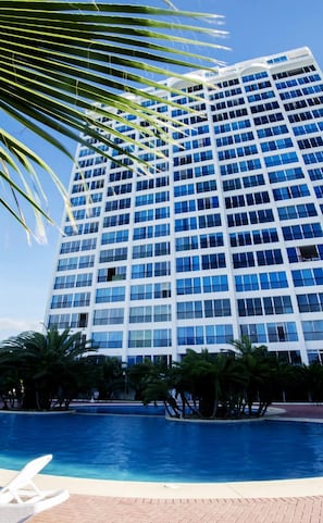 A high-rise hotel with a pool area, palm trees, and a clear blue sky.