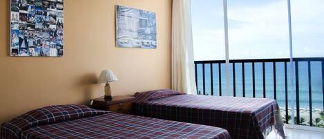A hotel room with two beds, a nightstand, a lamp, and a large window with a view of the ocean.