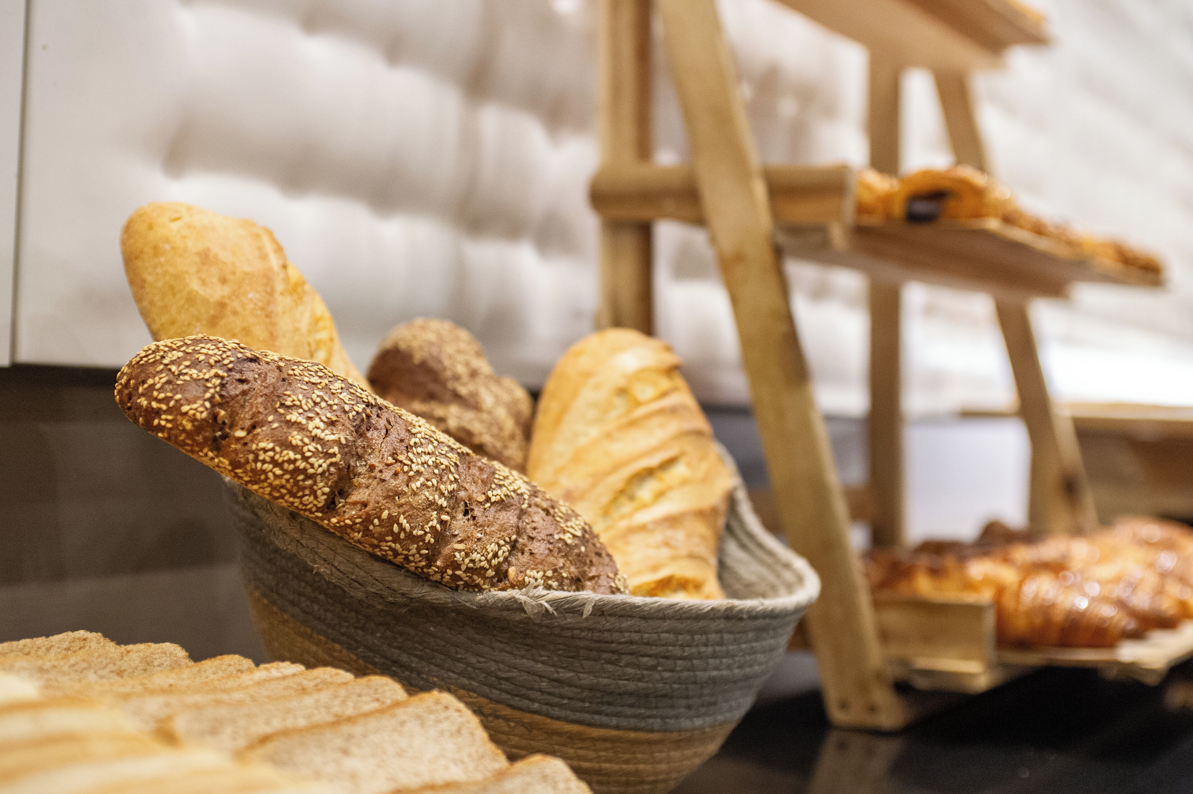 A basket filled with various types of bread, including a baguette and a loaf with sesame seeds.
