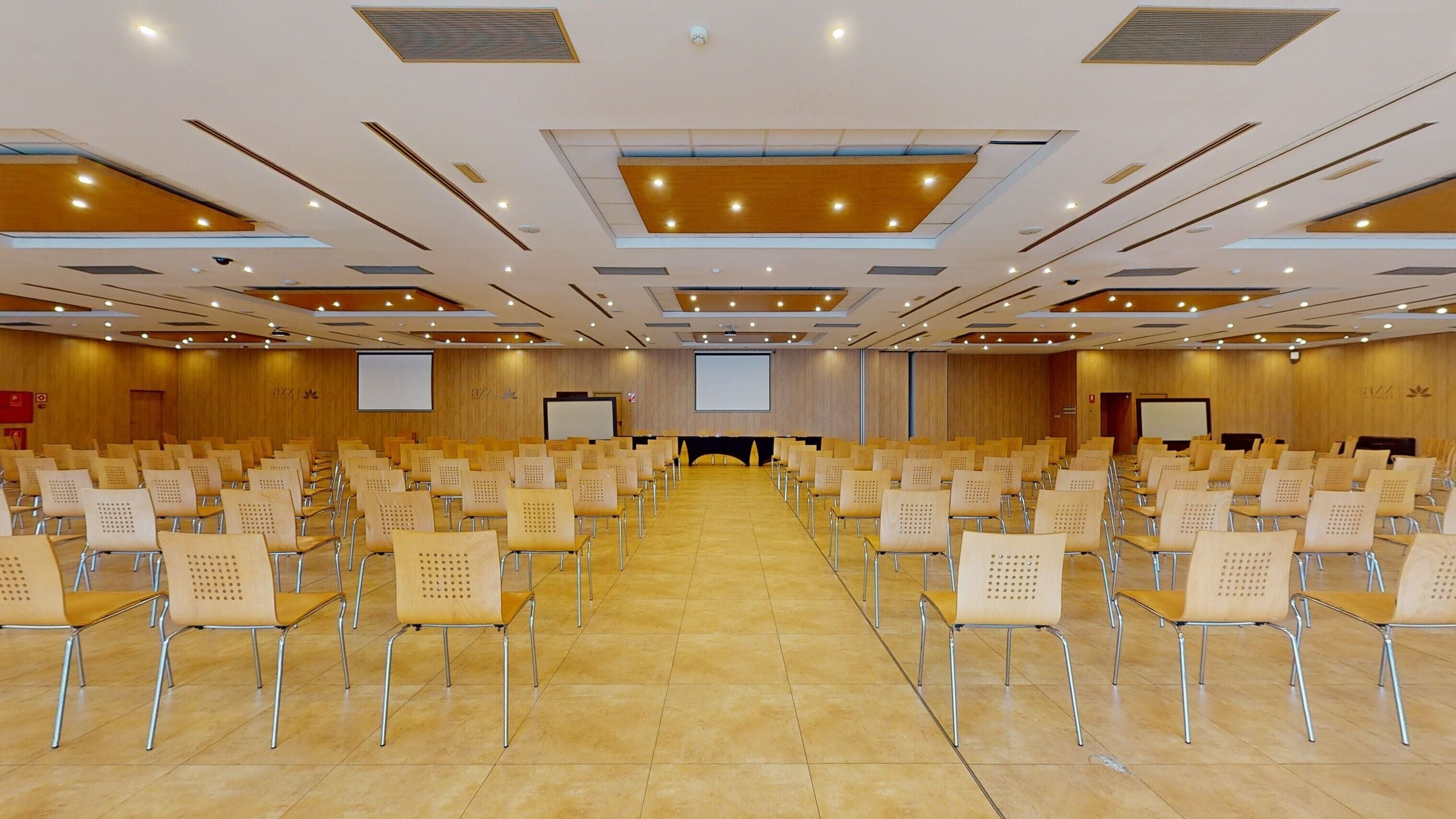 Une salle de conférence avec des rangées de chaises, une scène et un grand écran.