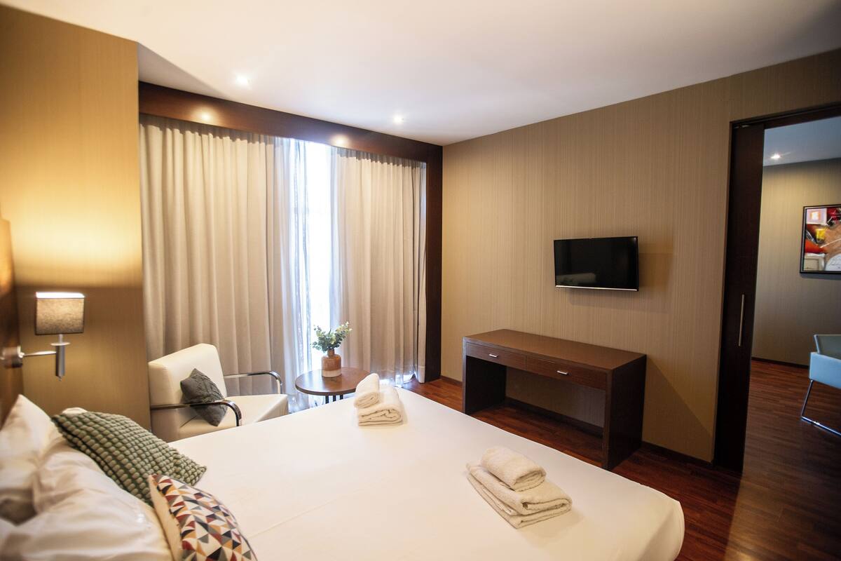 A hotel room with a bed, a desk, a chair, a TV, and a window with curtains.
