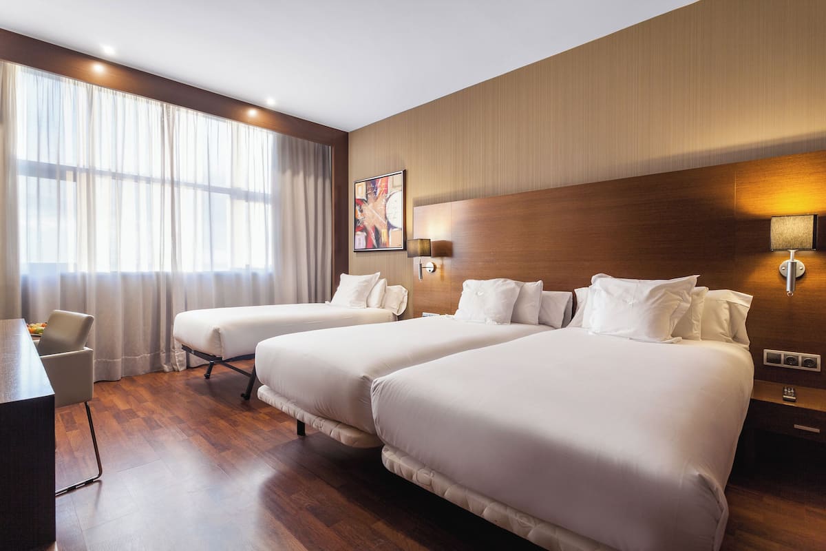 A hotel room with two beds, a desk, and a chair.