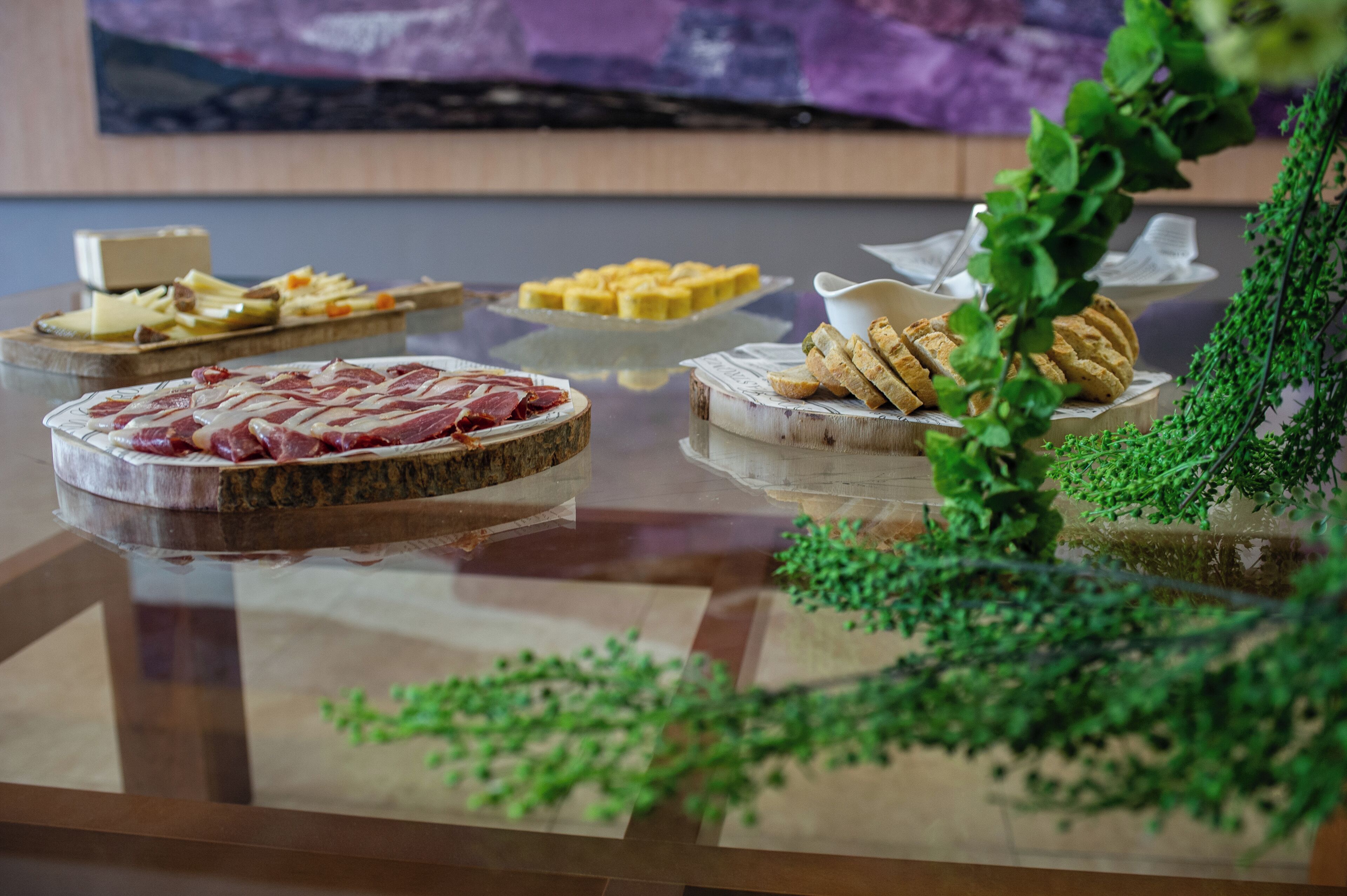 A glass-top table with various food items, including cheese, cured meats, and bread, arranged on wooden boards.