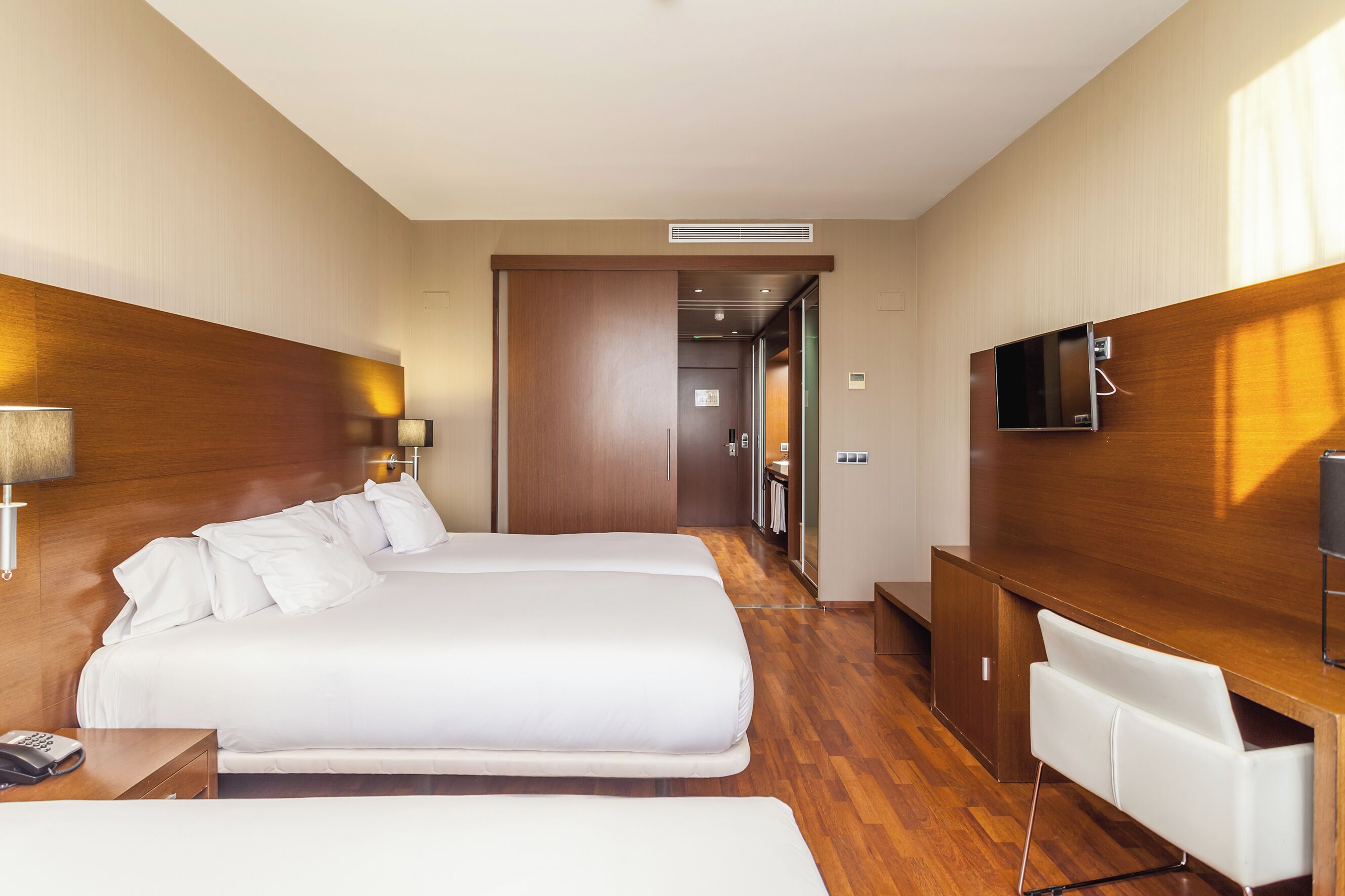Hotelkamer met twee bedden, een bureau, een stoel, een televisie en een badkamer zichtbaar door een open deur.