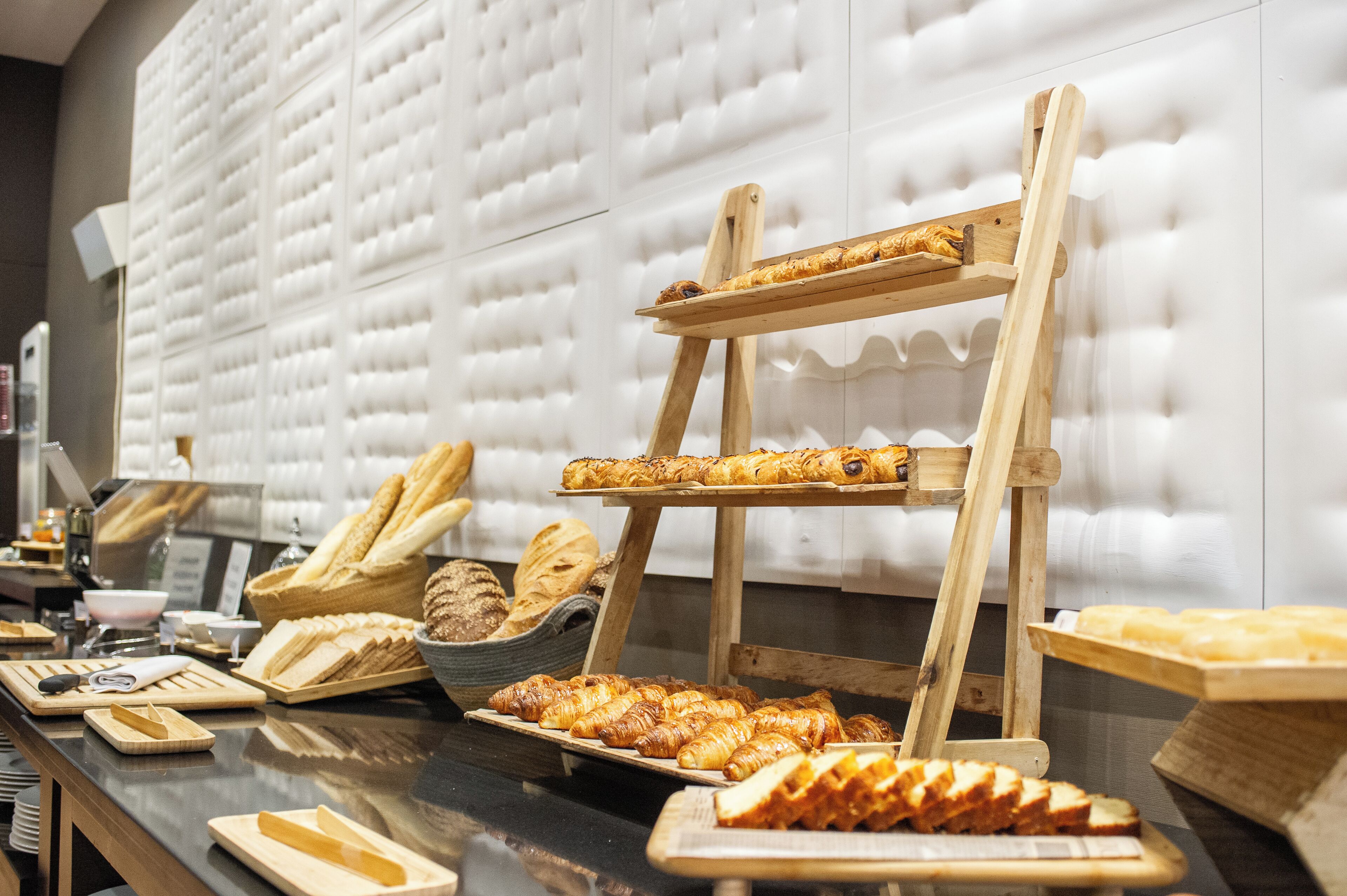 Un bufé con diversas opciones de panadería expuestas en pedestales y bandejas de madera.