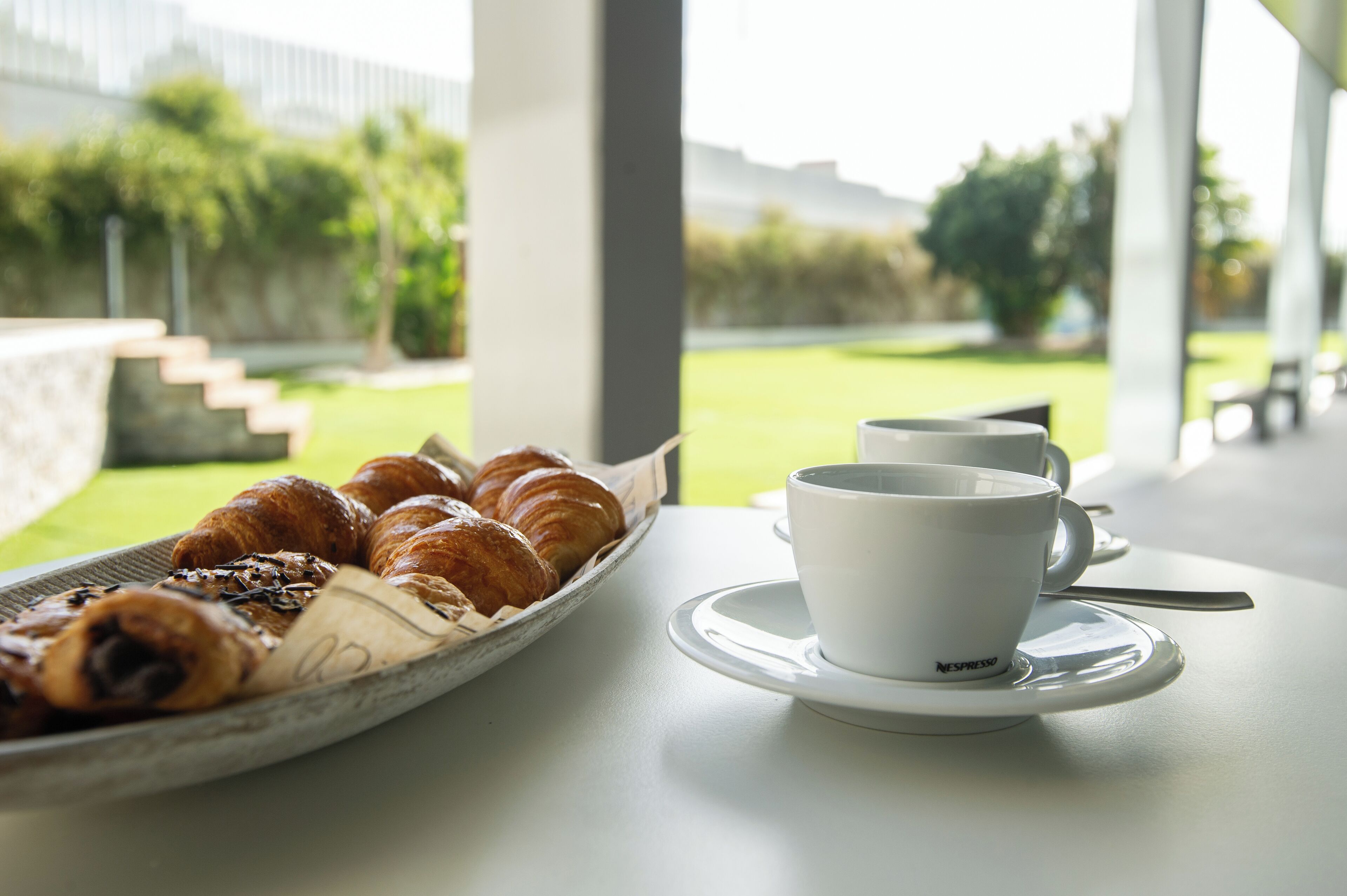 A table with croissants and a cup of coffee, overlooking a garden.