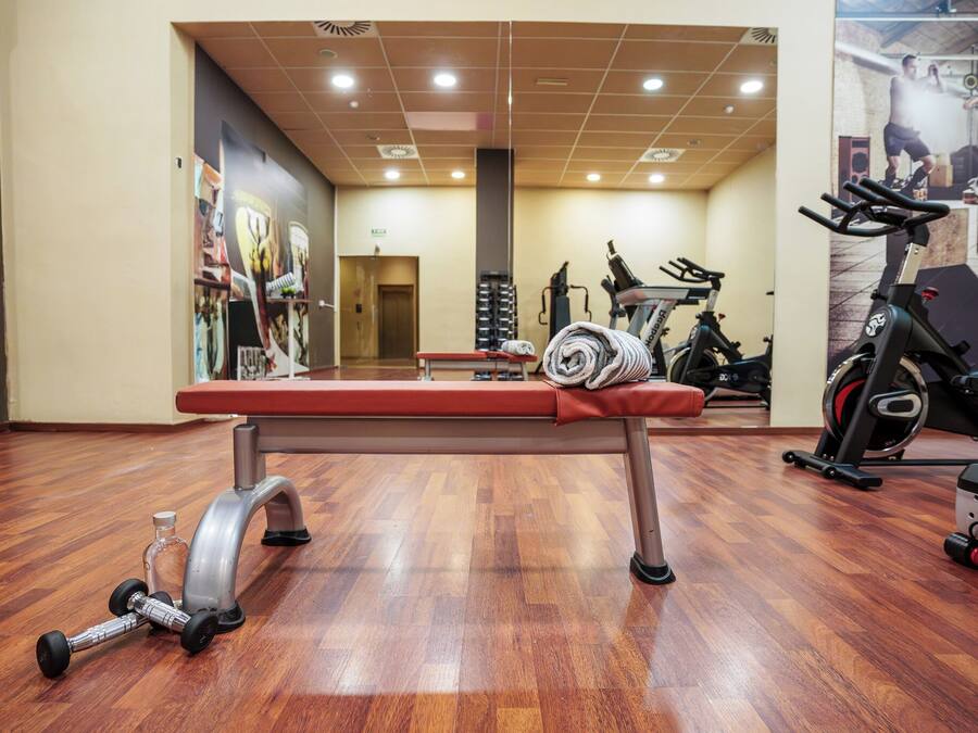 Un gimnasio con suelo de madera, equipamiento de ejercicio y una banca.