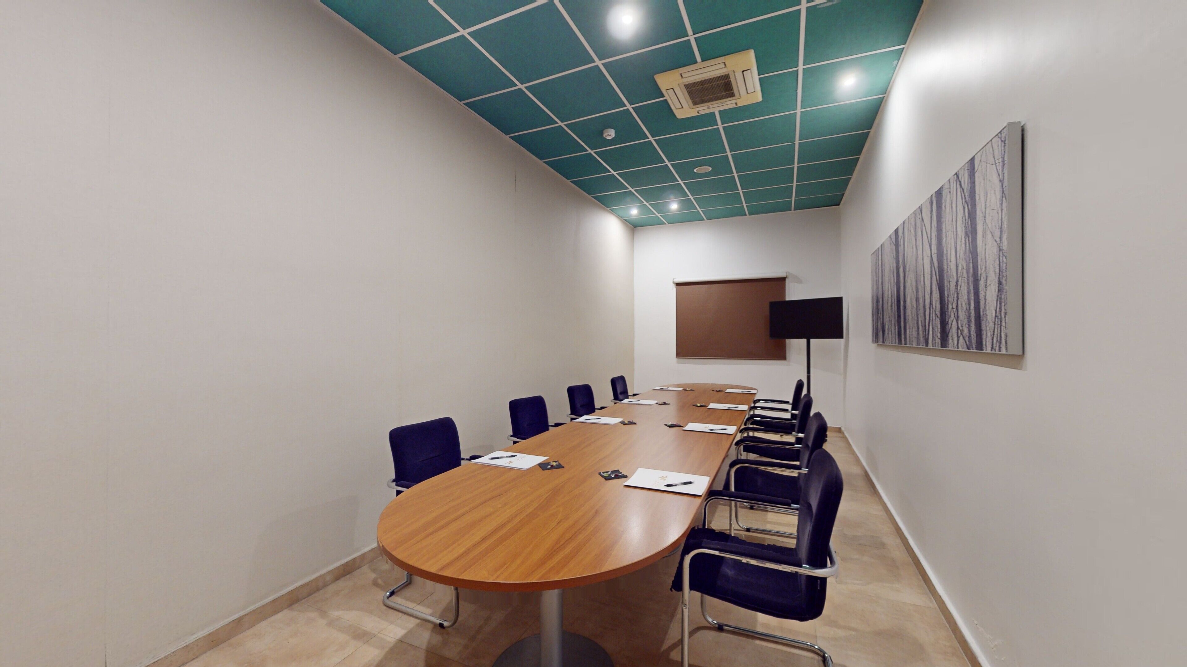 A conference room with a long table, chairs, a projector screen, and a painting on the wall.