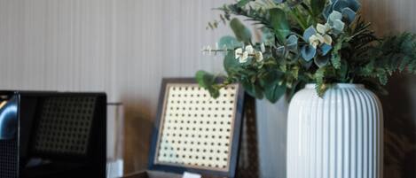 A room with a large white vase with green foliage, a framed picture, and a black box with a white object inside.