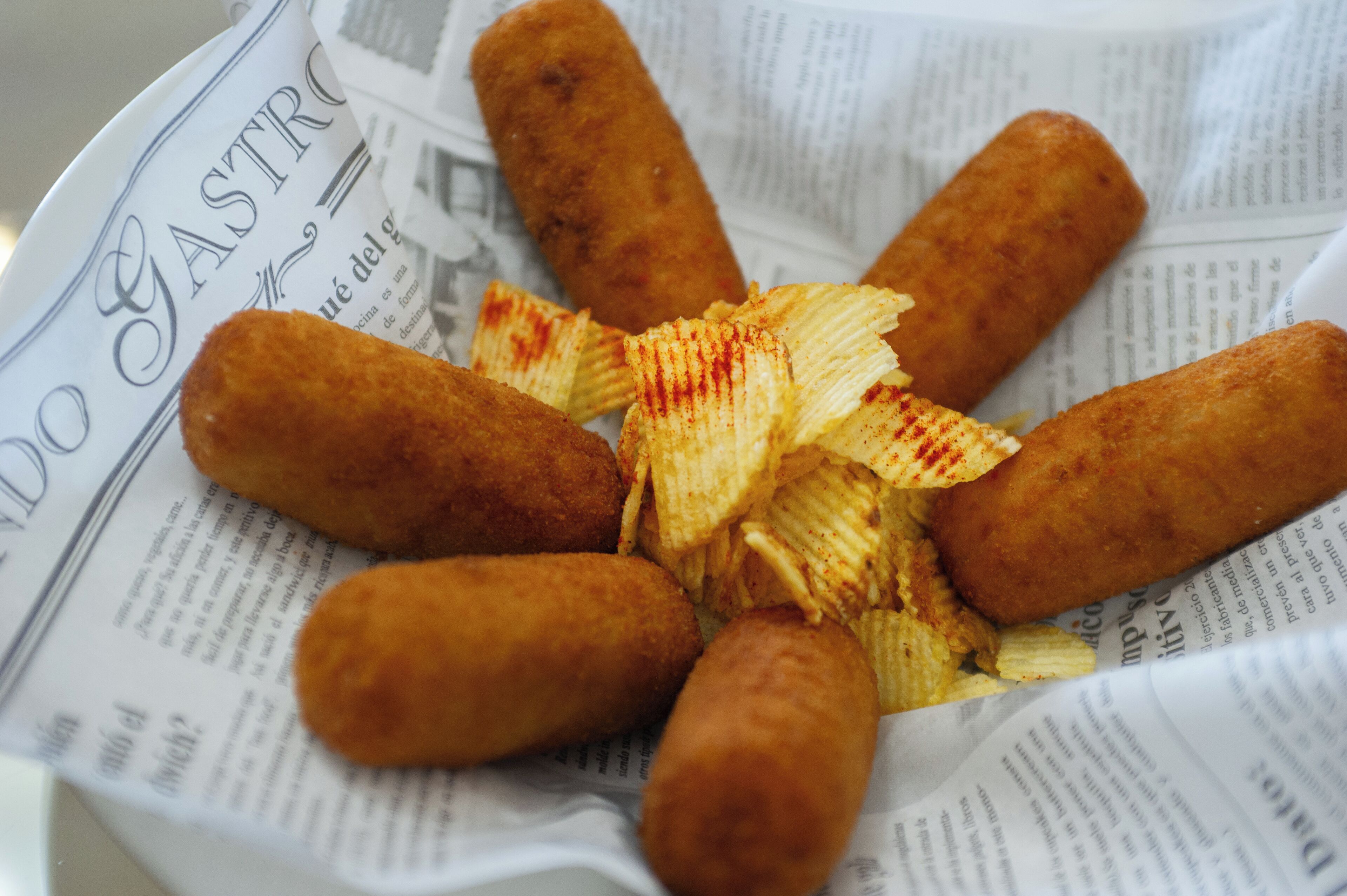 A plate of fried food items, possibly croquettes, on a newspaper.