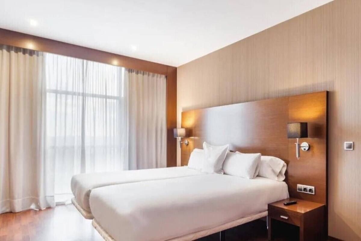 A hotel room with a large bed, two bedside tables, a nightstand, and a wall-mounted lamp.
