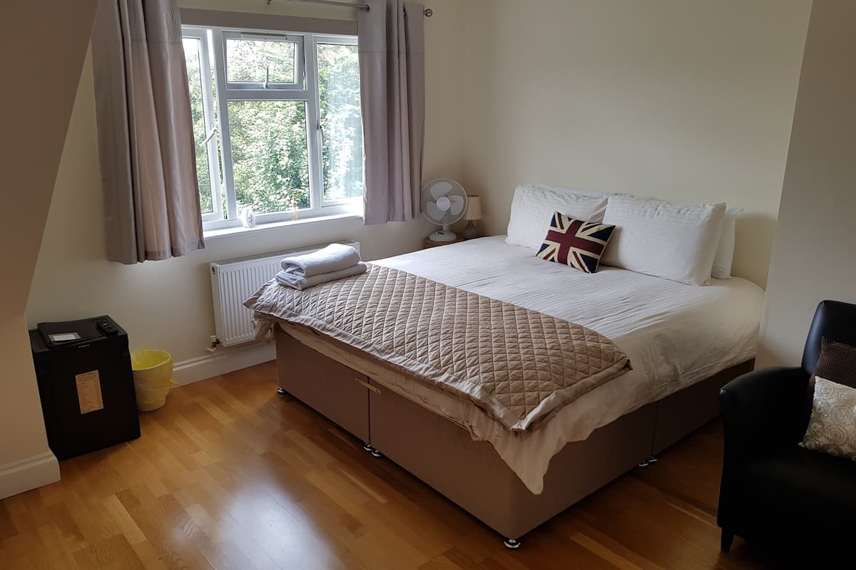 Ein Schlafzimmer mit Bett, einem Fenster mit Vorhängen, einem Heizkörper, einem Ventilator und einem Sessel.