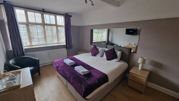 Habitación de hotel con cama, escritorio, silla, mesita de noche, espejo y ventana con cortinas.