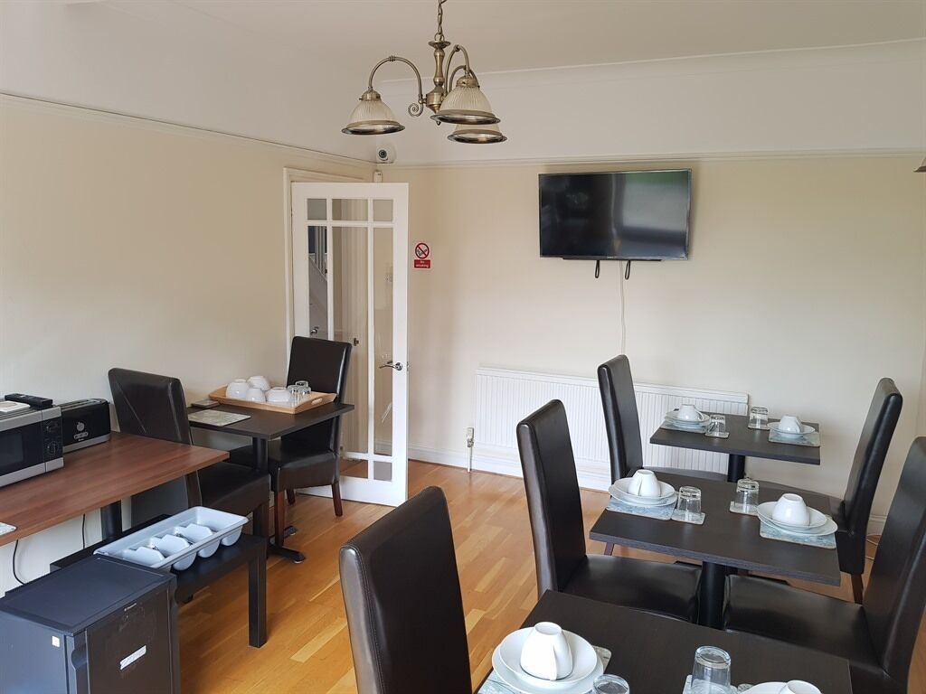A dining area with tables set for four, a television mounted on the wall, and a door leading to another room.
