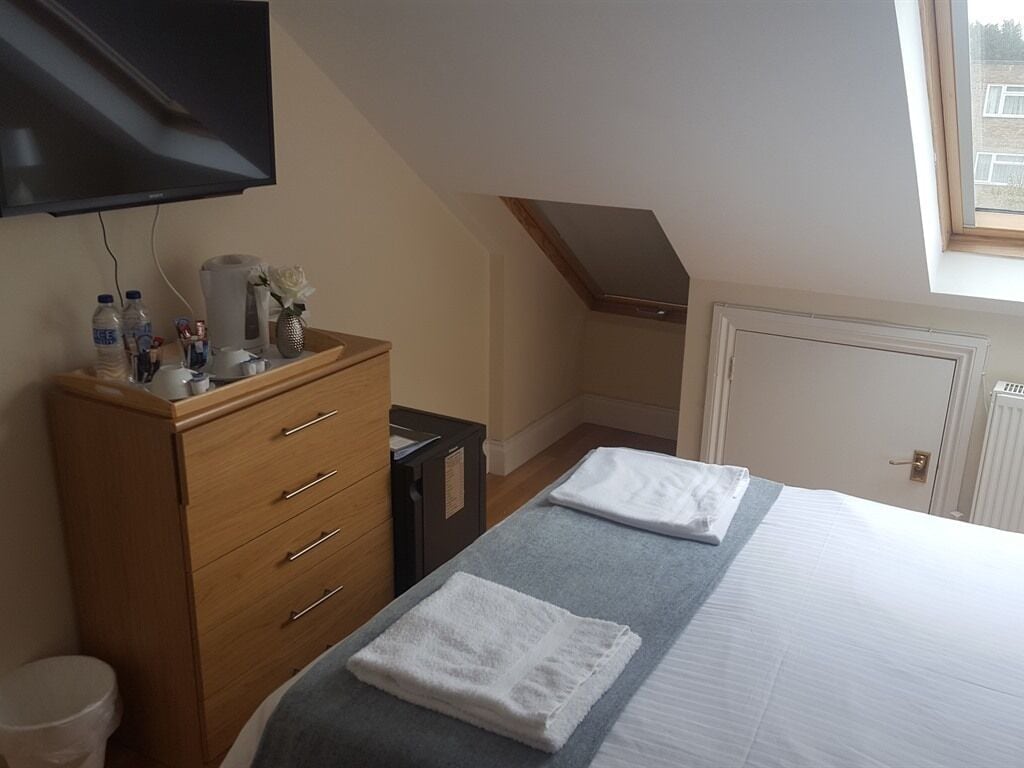 Ein Hotelzimmer mit Bett, einem Holzschrank, einem an der Wand befestigten Fernseher und einem Fenster, das natürliches Licht hereinlässt.