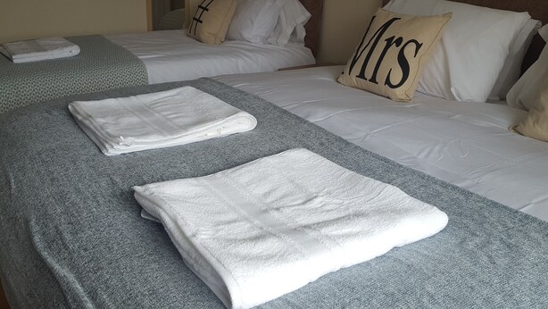 A hotel room with two beds, each with a pillow labeled "Mrs." and "Mr." and neatly folded white towels on the beds. - Kathleen House (Enfield)