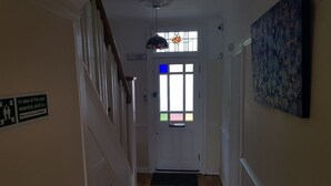A hallway with a white door, a stained glass window, and a black mat at the entrance. - Kathleen House (Enfield)